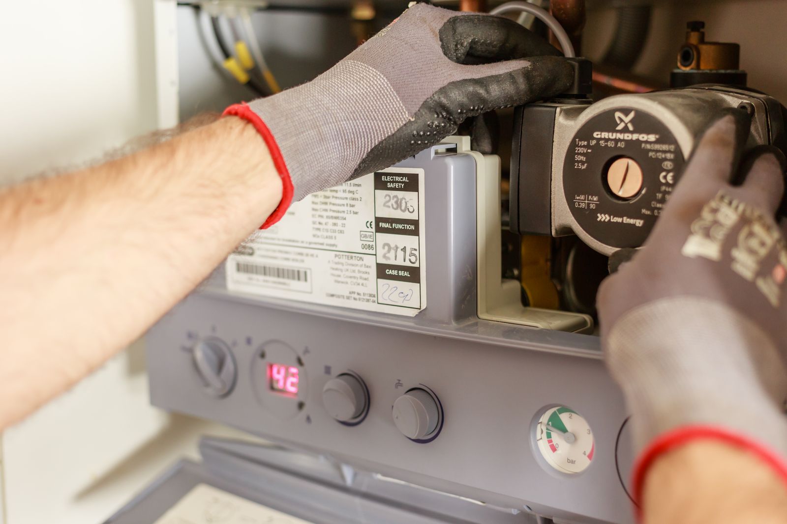 Gloved technician servicing the internal control panel and pump of a home heating boiler